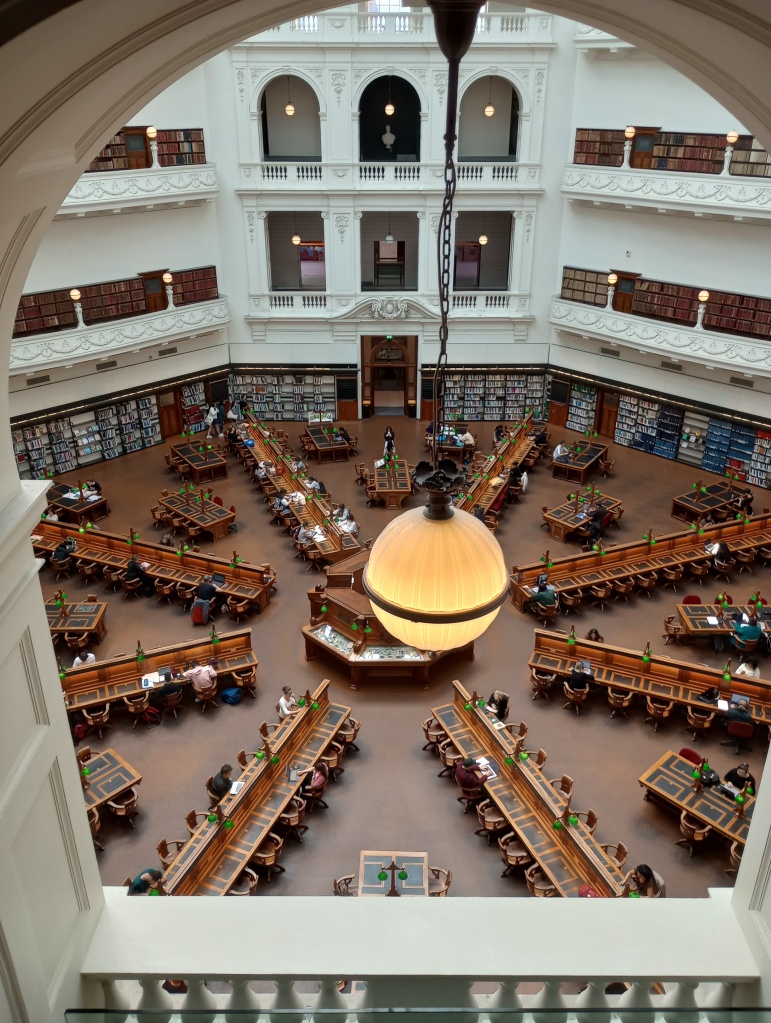 Der Hauptsaal der Bibliothek von einem Balkon aufgenommen. Der Raum ist rund und strahlenförmig von der Mitte aus, sind mehrere lange Tische mit Stühlen aufgestellt